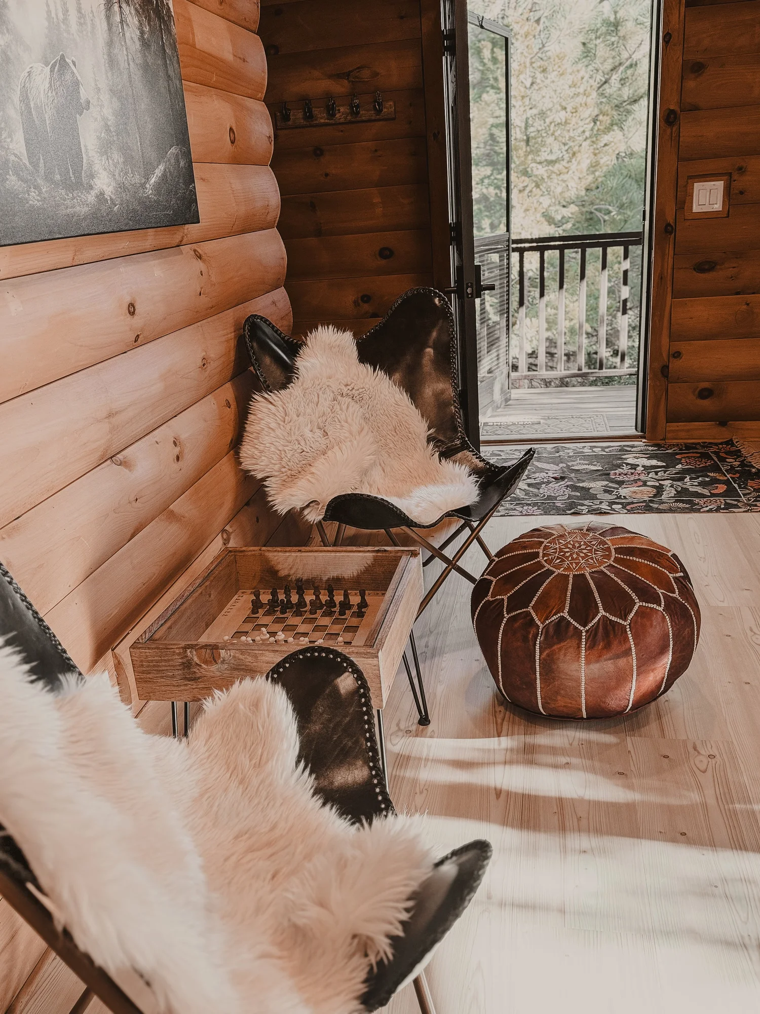 Reading nook with butterfly chairs, sheepskins and a leather pouf by the deck door at Dark Moon Chalet in Julian, designed by Salt and Sky Lodging Co.