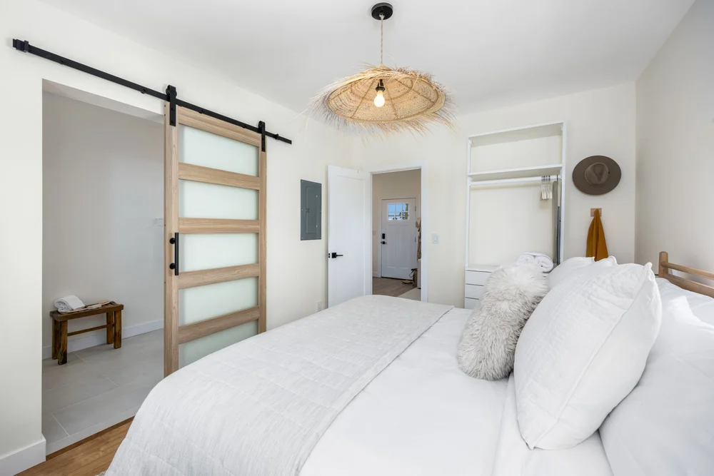 The bedroom with a sliding barn door to the bathroom and a woven pendant in Unit Three at The Swell, Oceanside