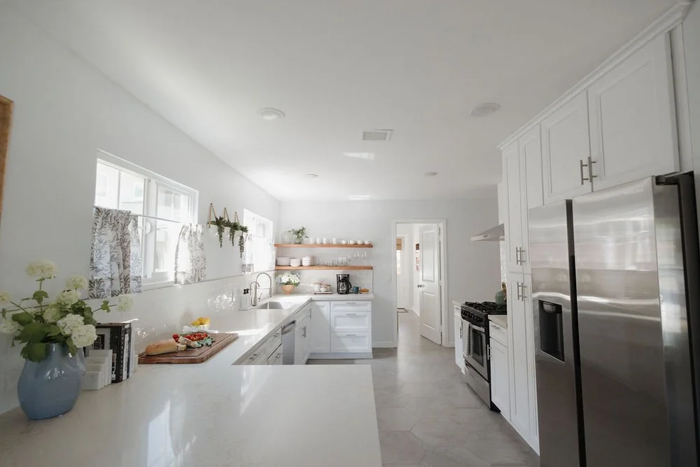 The long white kitchen in The Villa with open shelves and a stainless fridge