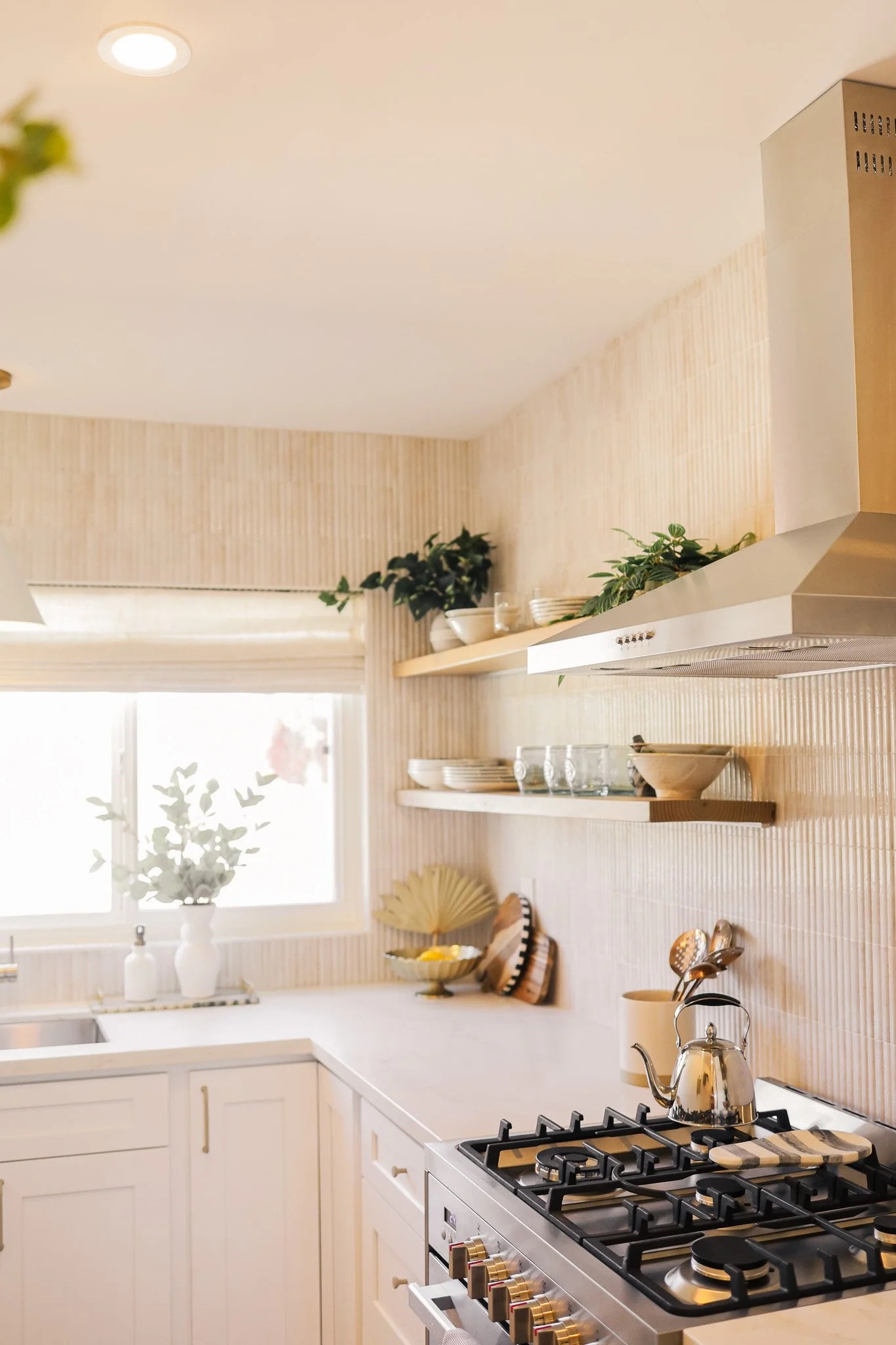 Kitchen with a range hood, floating shelves and a gas range at Clementine C in Oceanside, designed by Salt and Sky Lodging Co.
