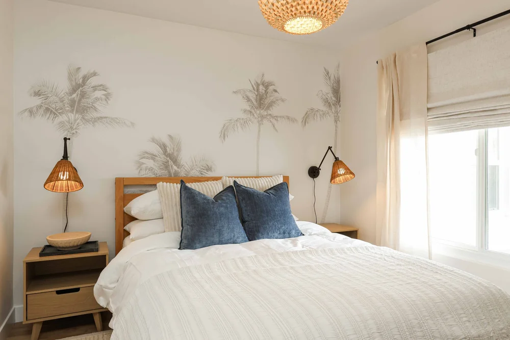 The second bedroom with navy pillows, a palm mural and a rattan wall sconce in Unit One at The Swell, Oceanside