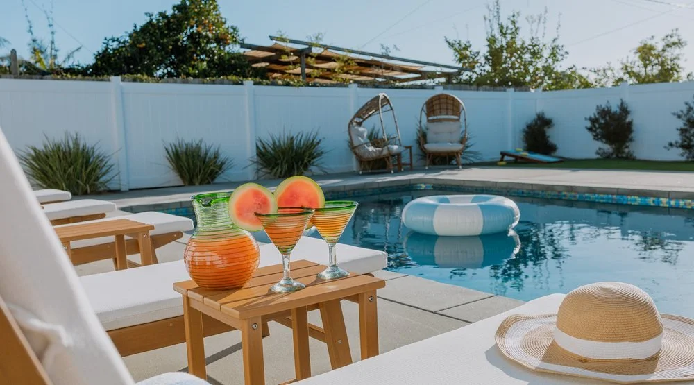 A styled backyard pool at a short term rental we manage, with loungers, a float and drinks set out on a side table