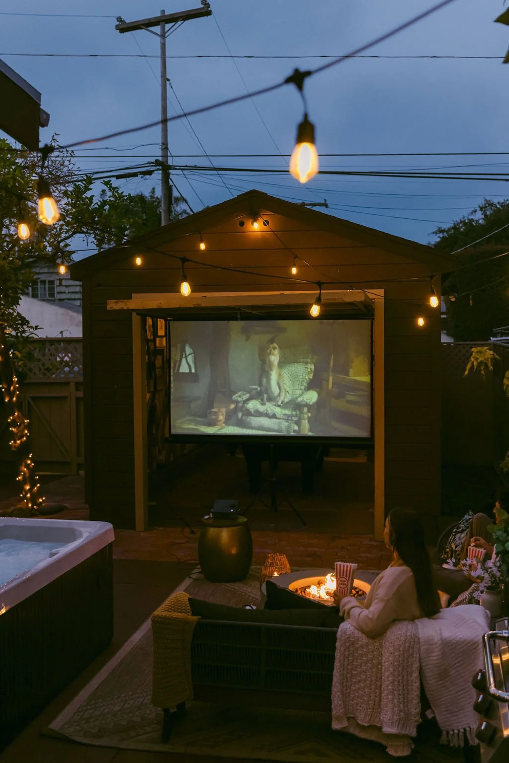 Movie night on the outdoor projector under string lights in the backyard at Palm Parkside, with the hot tub beside it