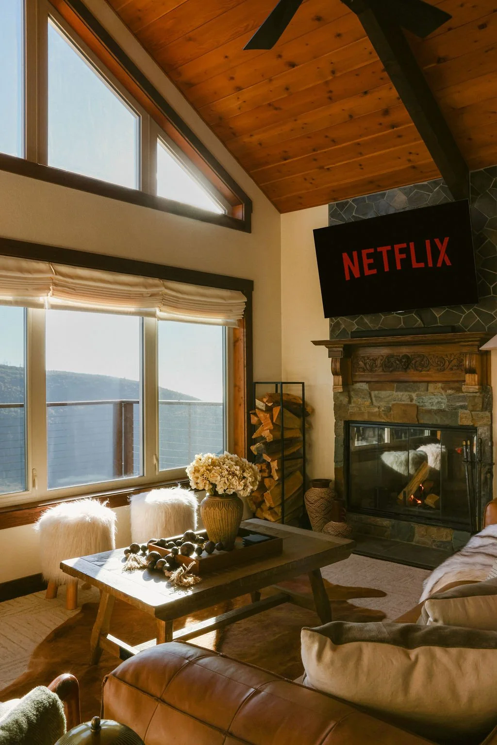 Living room with a leather sofa, fireplace and large windows under a wood ceiling