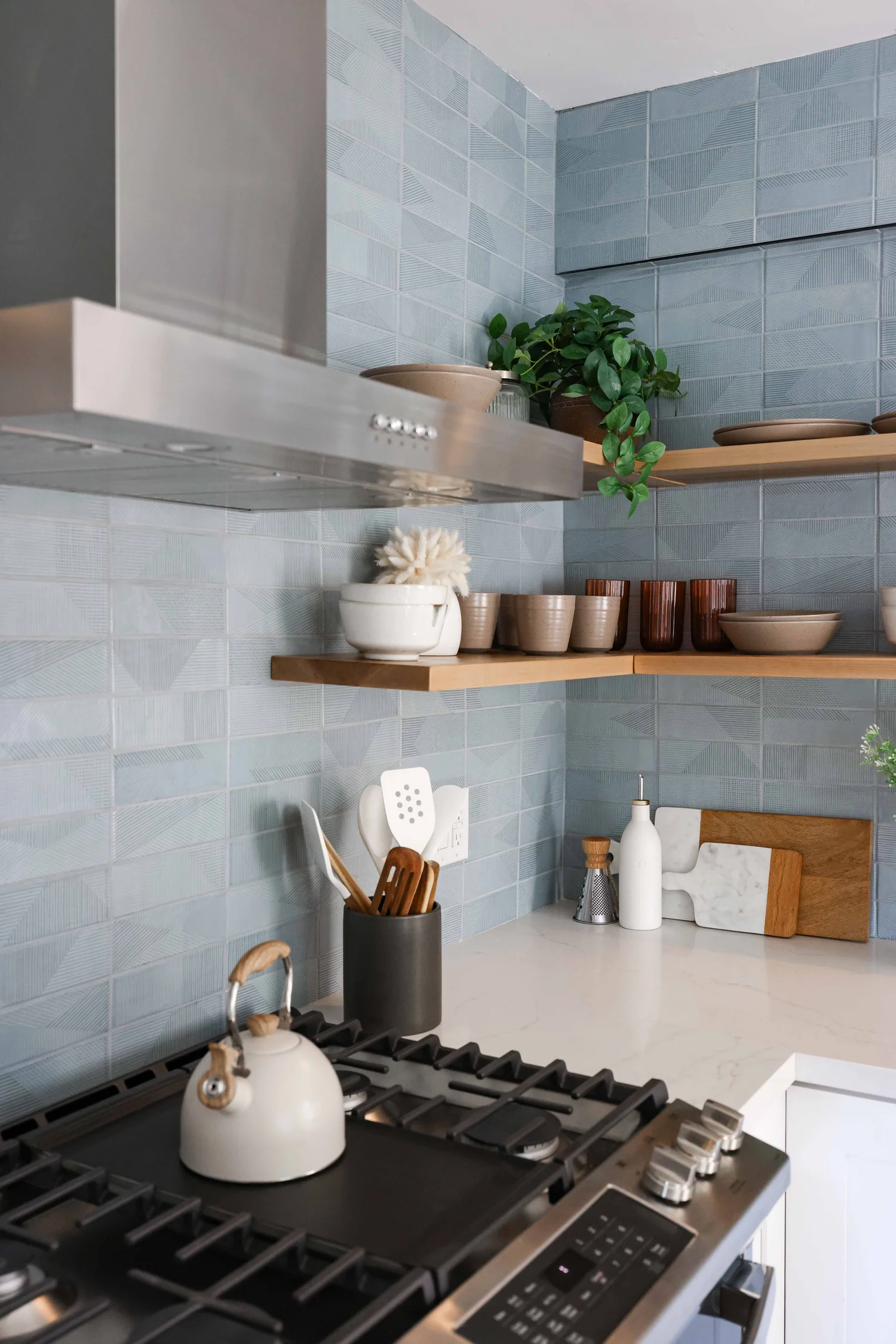 Kitchen with blue tile walls, floating wood shelves and a gas range at Clementine A in Oceanside, designed by Salt and Sky Lodging Co.