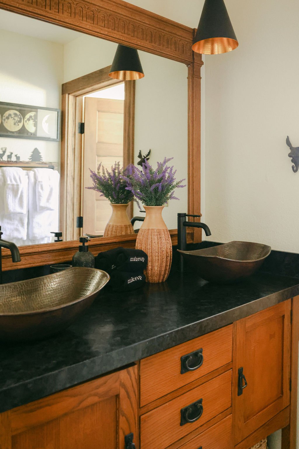 Bathroom vanity with two vessel sinks, a black counter and wood cabinets