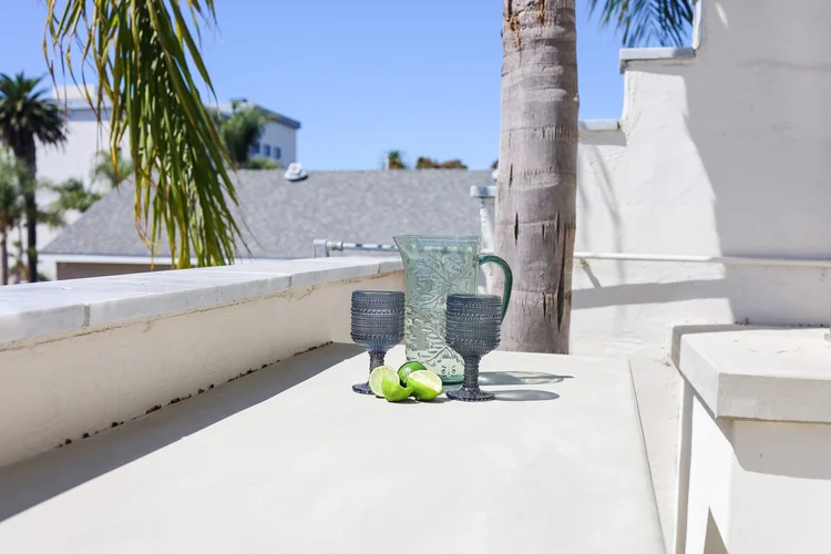 A glass pitcher and two glasses with lime slices on the patio ledge at The Swell, with a palm tree and blue sky behind