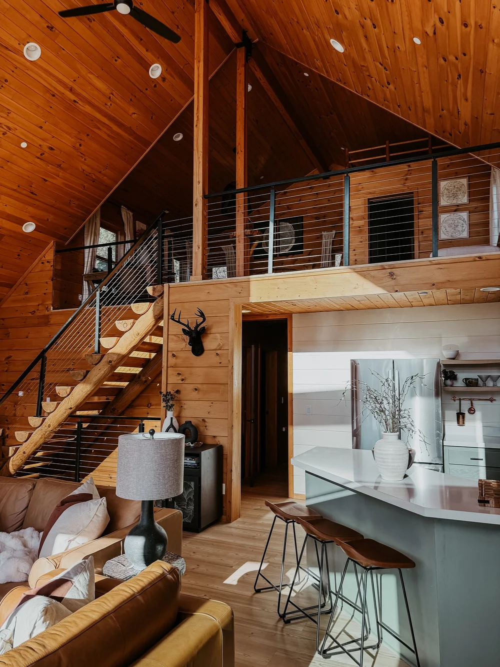 Great room with a log staircase, loft railing and kitchen island at Dark Moon Chalet in Julian, designed by Salt and Sky Lodging Co.