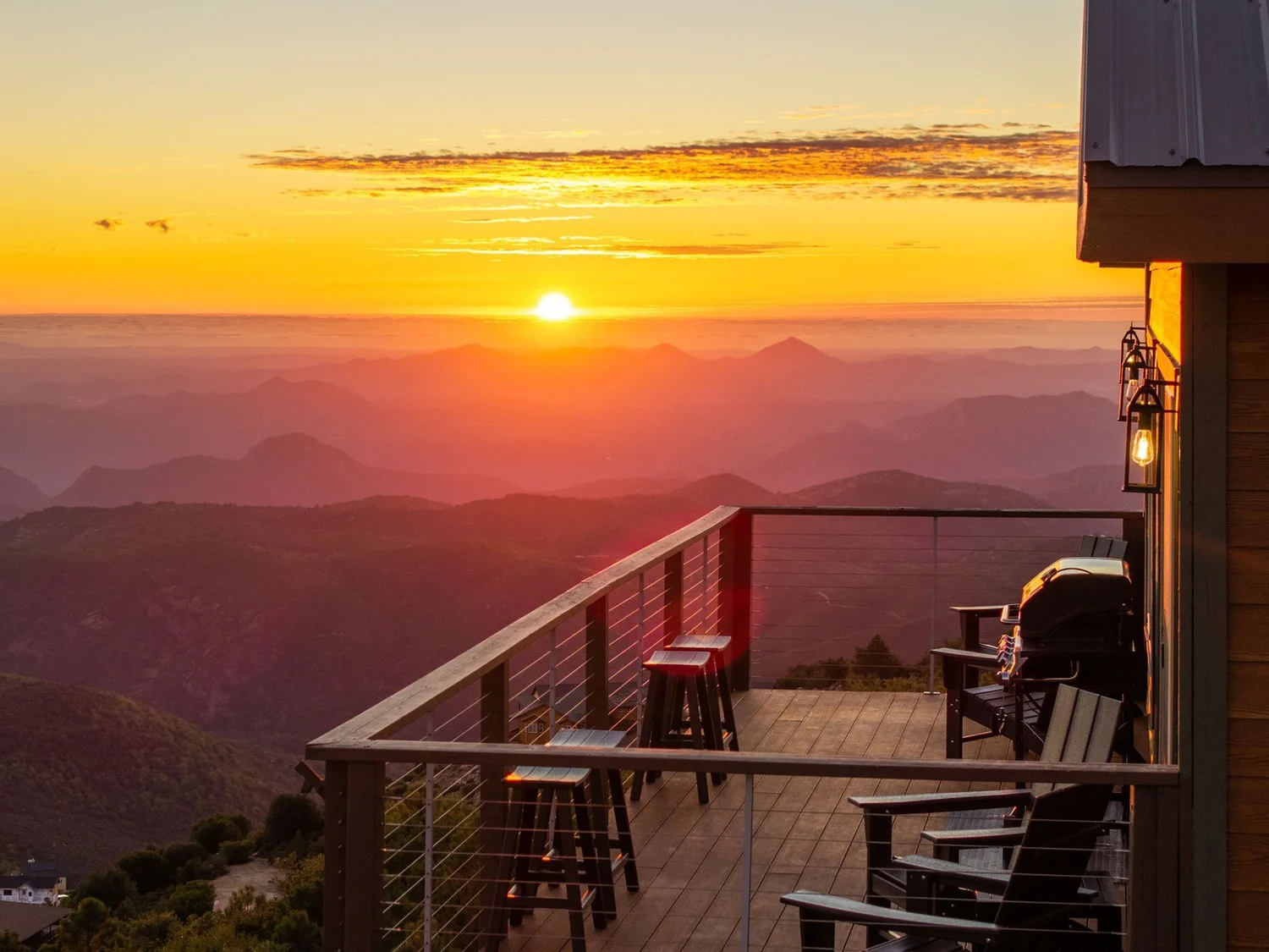 The sun setting over layered ridgelines from the deck at Wild Moon Ranch near Julian, with bar stools, chairs and lantern light