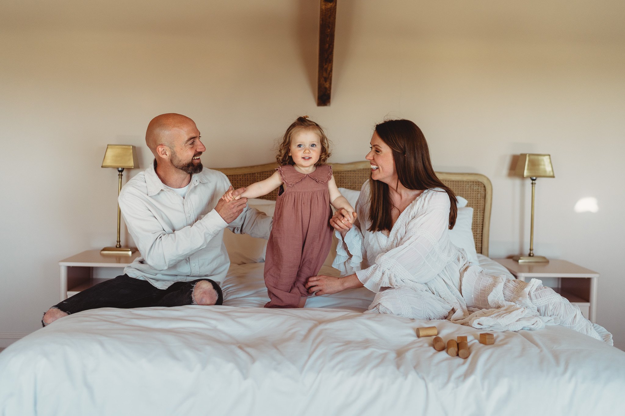 A toddler jumping on the bed with mum and dad during a family session in Swansea South Wales