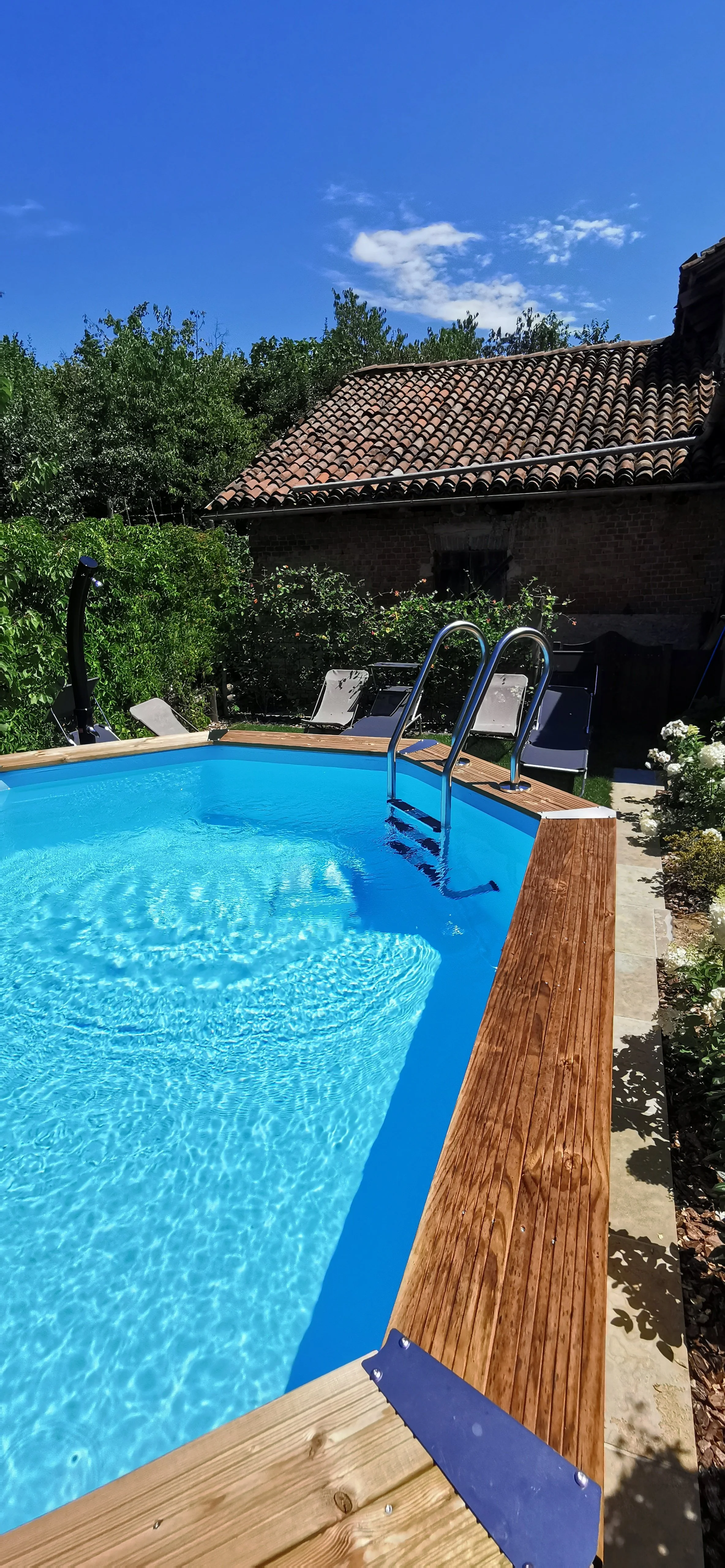 Piscina privata in giardino, con gradini in metallo, sedie a sdraio sui bordi e case con tetti in terracotta sullo sfondo