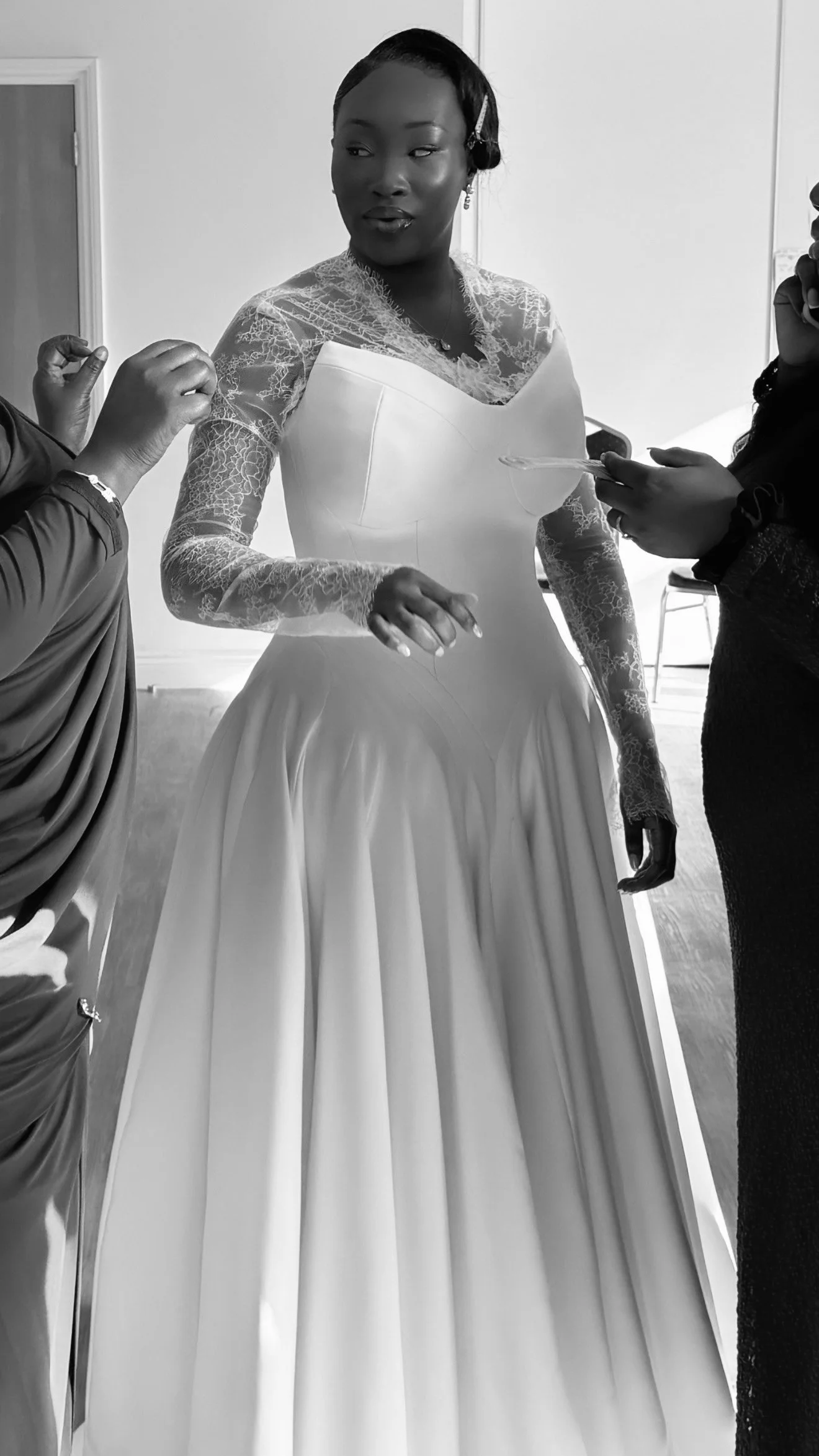 A woman in a wedding dress surrounded by people during a wedding preparation or fitting.