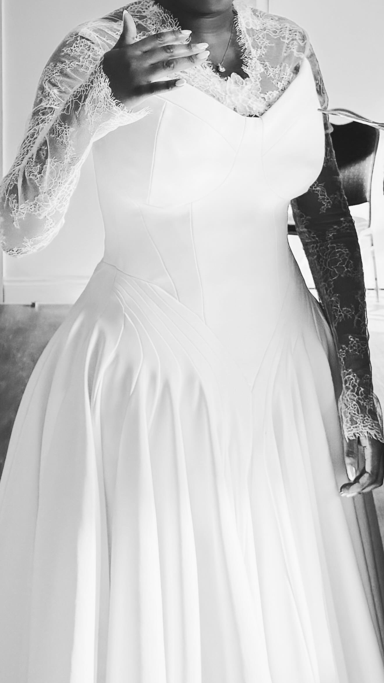 A woman taking a mirror selfie wearing a wedding dress with lace sleeves.