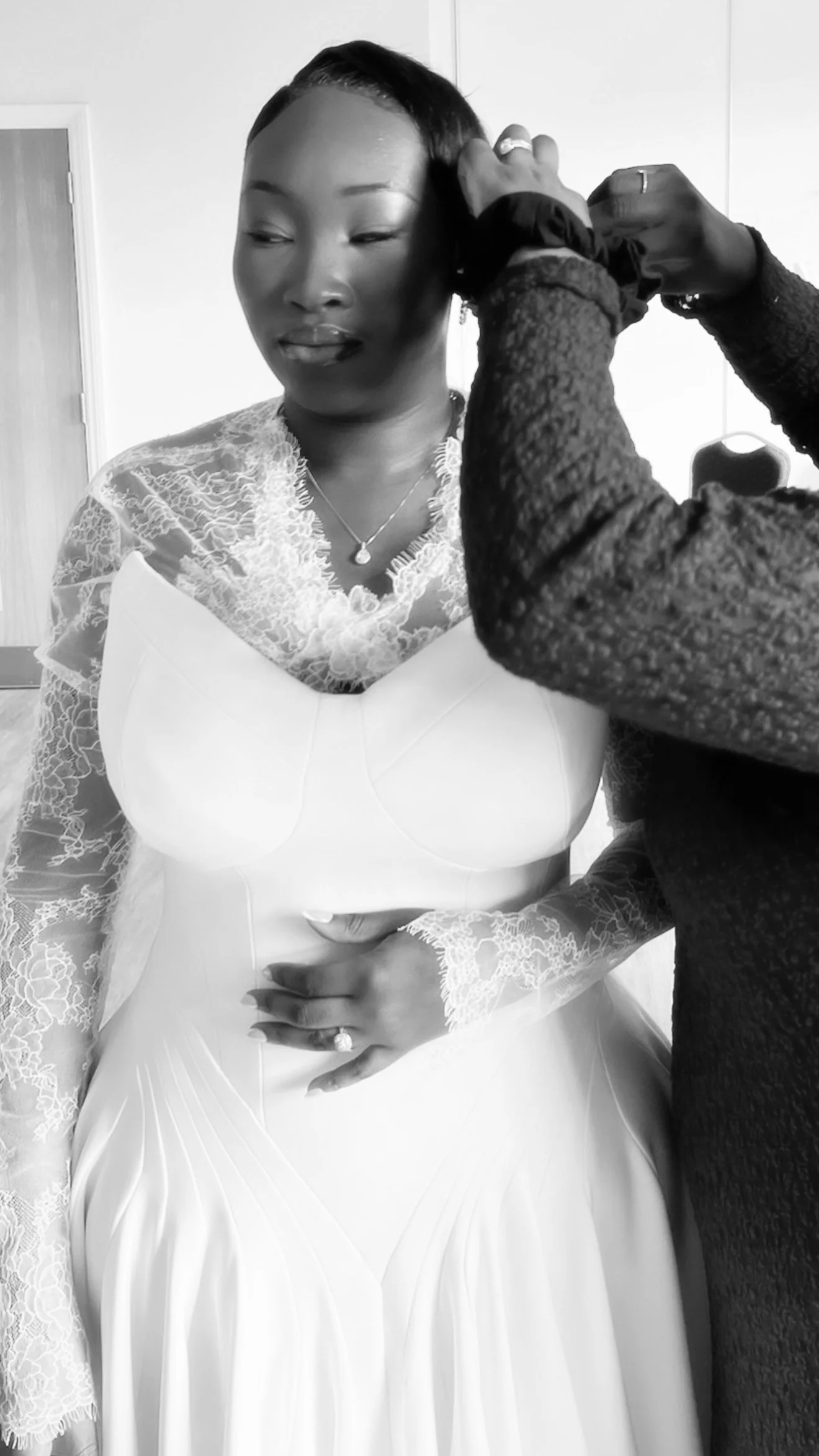 A woman in a wedding dress gets her hair styled by another person. The scene is in black and white.
