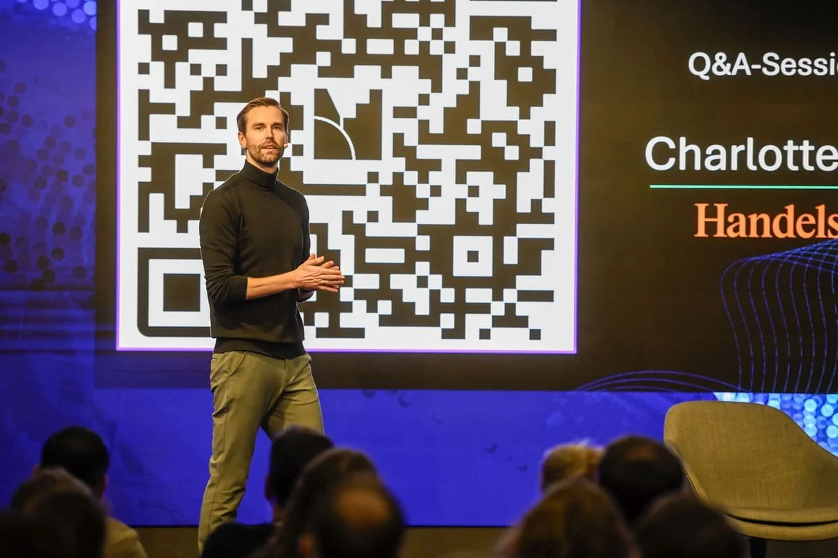 Ralf Leister moderiert ein Event interaktiv und steht vor einem QR-Code.