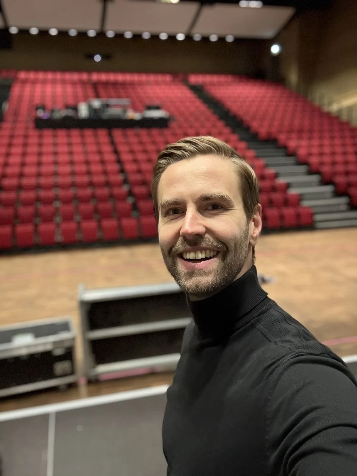 Ein Selfie eines jungen Mannes auf einer Bühne Richtung Publikum. Die Sitze sind leer. Er ist für die Eventmoderation verantwortlich.