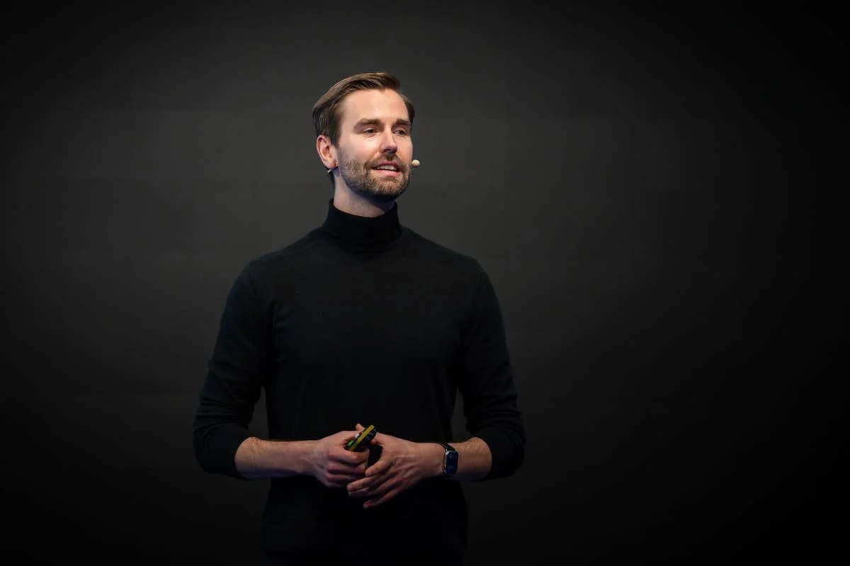 Ein junger Mann steht auf einer Bühne vor schwarzem Hintergrund am Anfang einer Präsentation