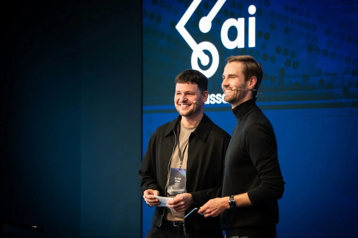 Zwei junge Männer stehen auf der Bühne und lachen Richtung Publikum während der Eventmoderation