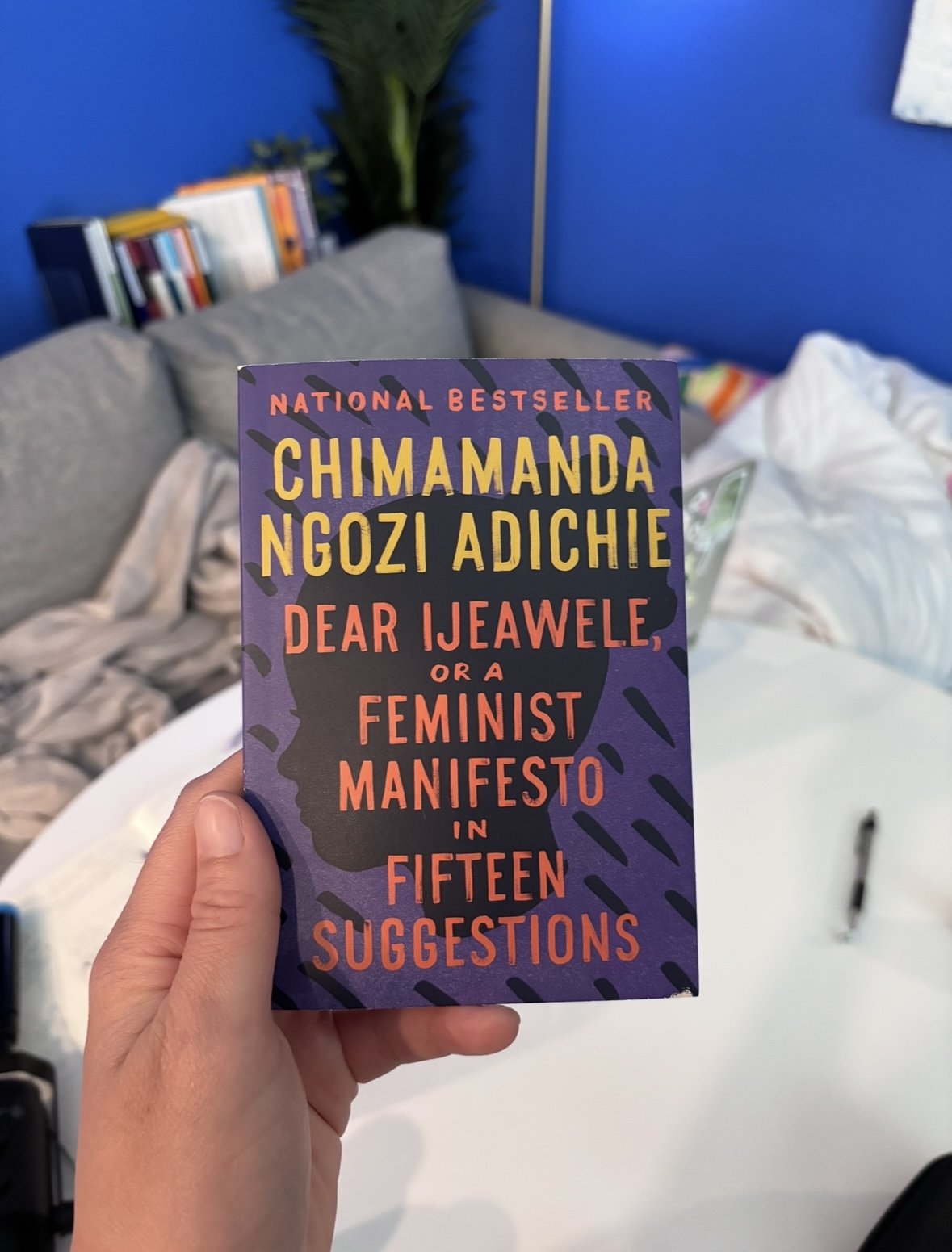 A picture of a person holding Chimamanda Ngozi Adichie's book called "Dear Ijeawele, or a Feminist Manifesto in Fifteen Suggestions"