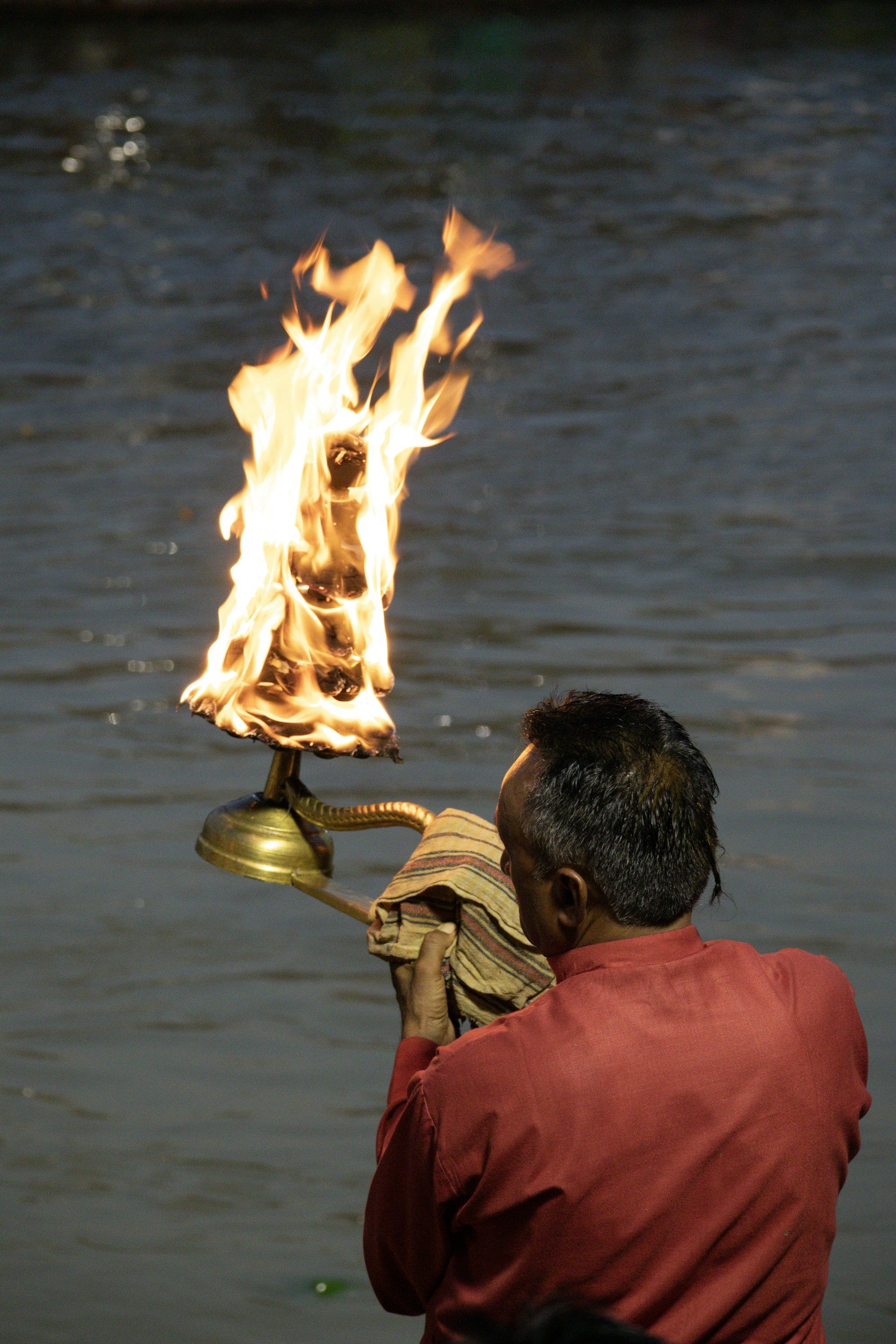 A man in a red shirt holding a lit flame over a water background.