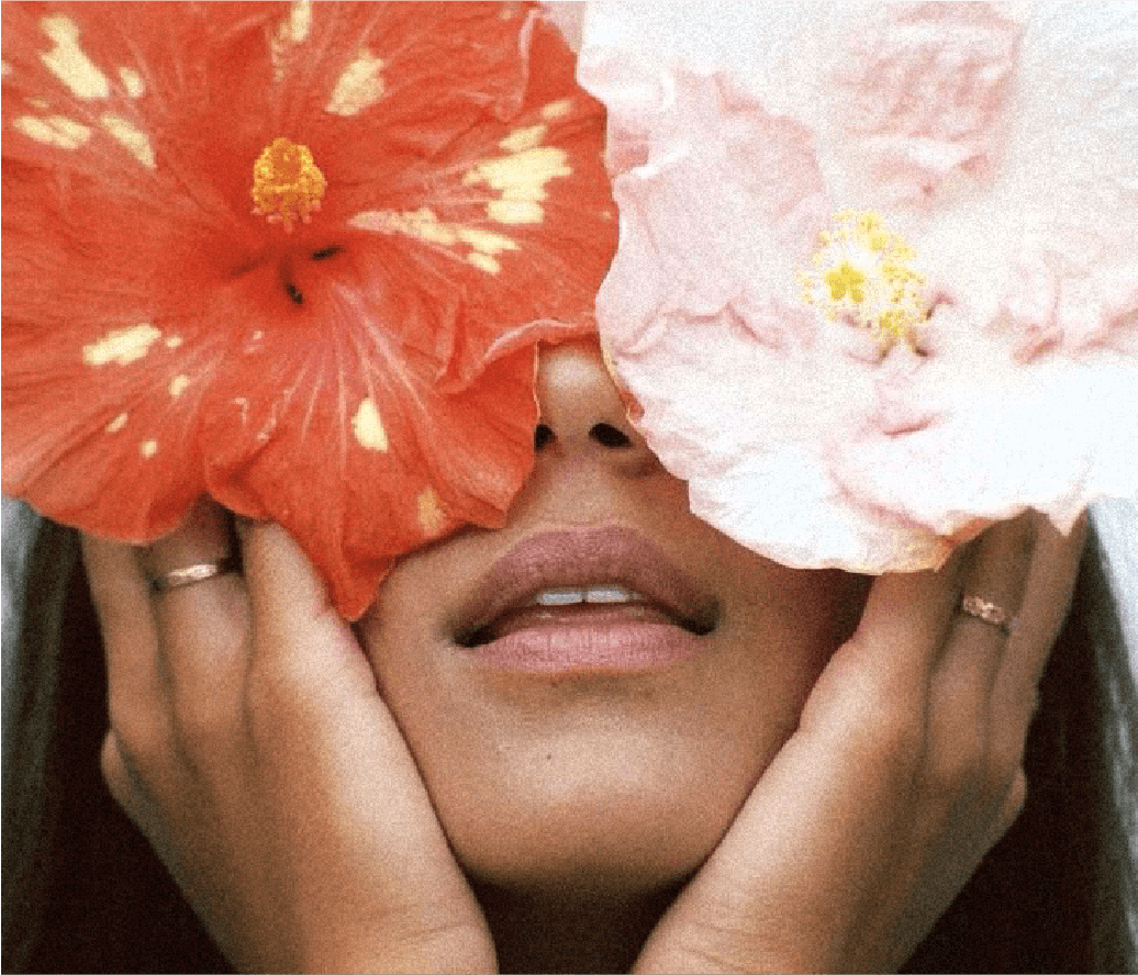 Une personne tenant deux fleurs imposantes devant ses yeux, laissant seulement sa bouche visible.