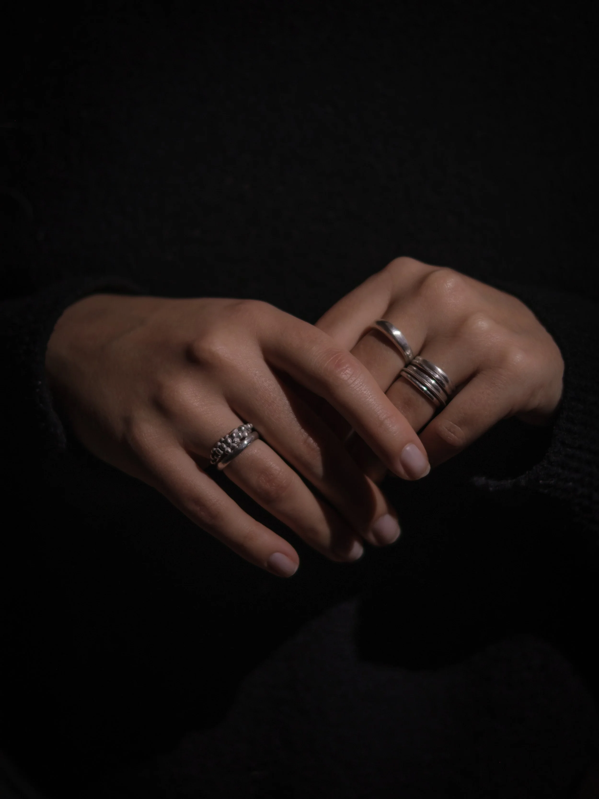 Close-up of two hands with multiple rings, set against a dark background.