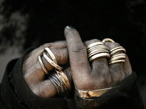 Close-up of multiple rings on fingers and hand, with black and dark background.