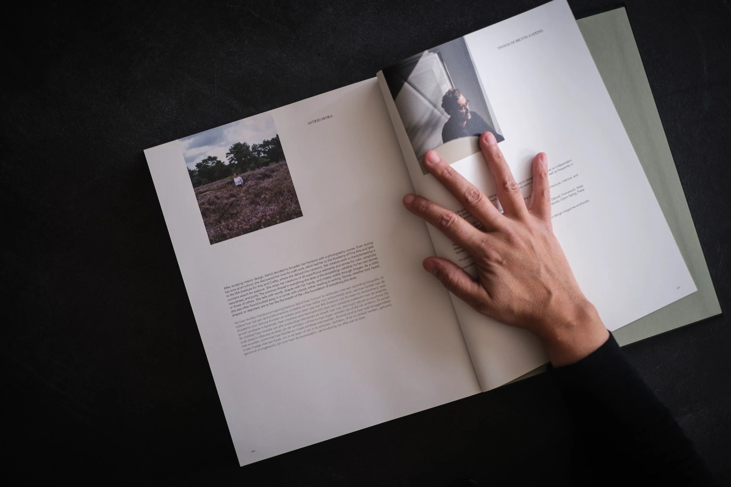 Open magazine on a black surface, showing two pages with images and text. One page has a photo of a person standing in a purple flower field; the other page has a portrait of a woman with short hair and glasses.
