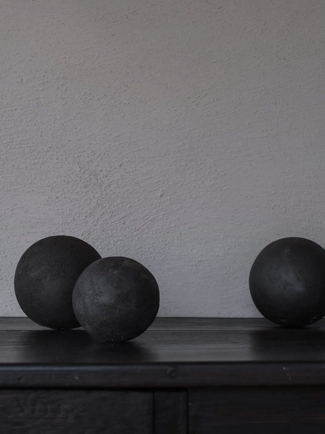 Three black spherical objects placed on a dark wooden surface against a light textured wall background.