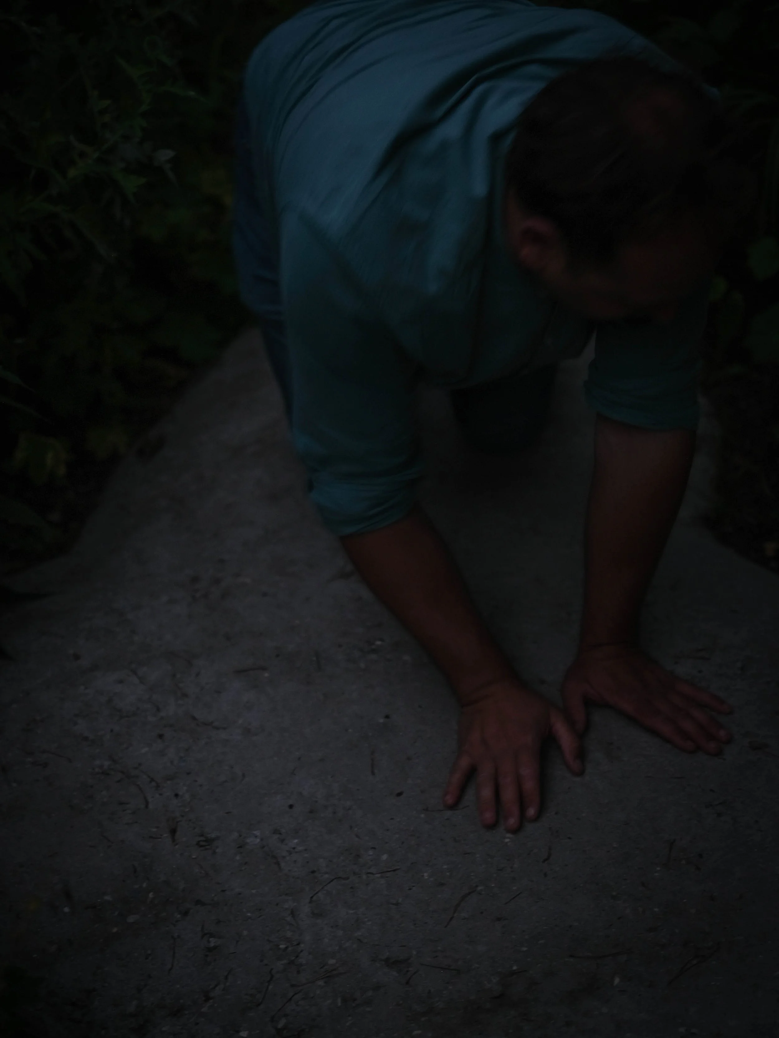 A person in a blue shirt crawling on the ground in a dark outdoor setting.
