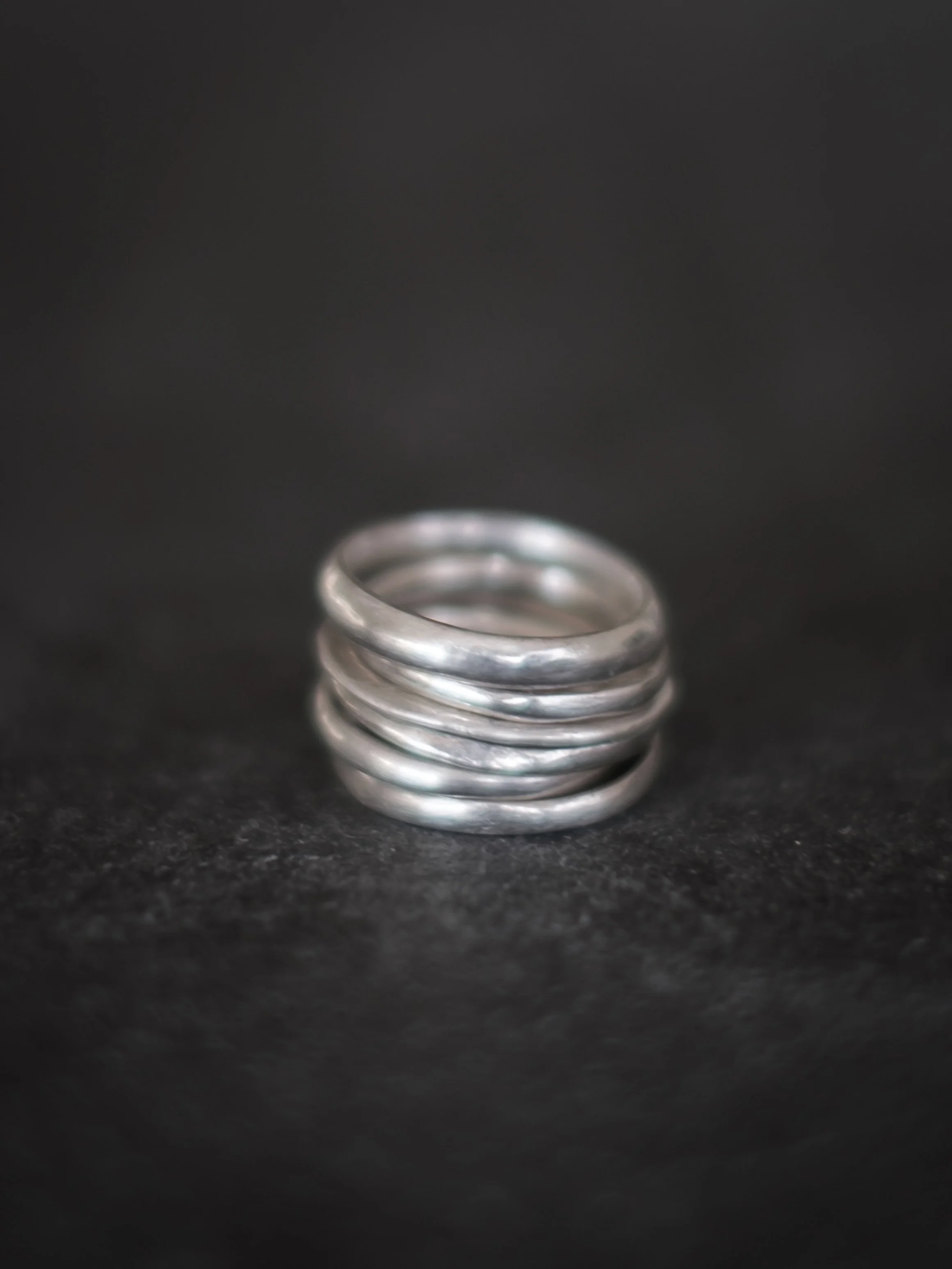 A close-up of four stacked silver rings on a black surface.