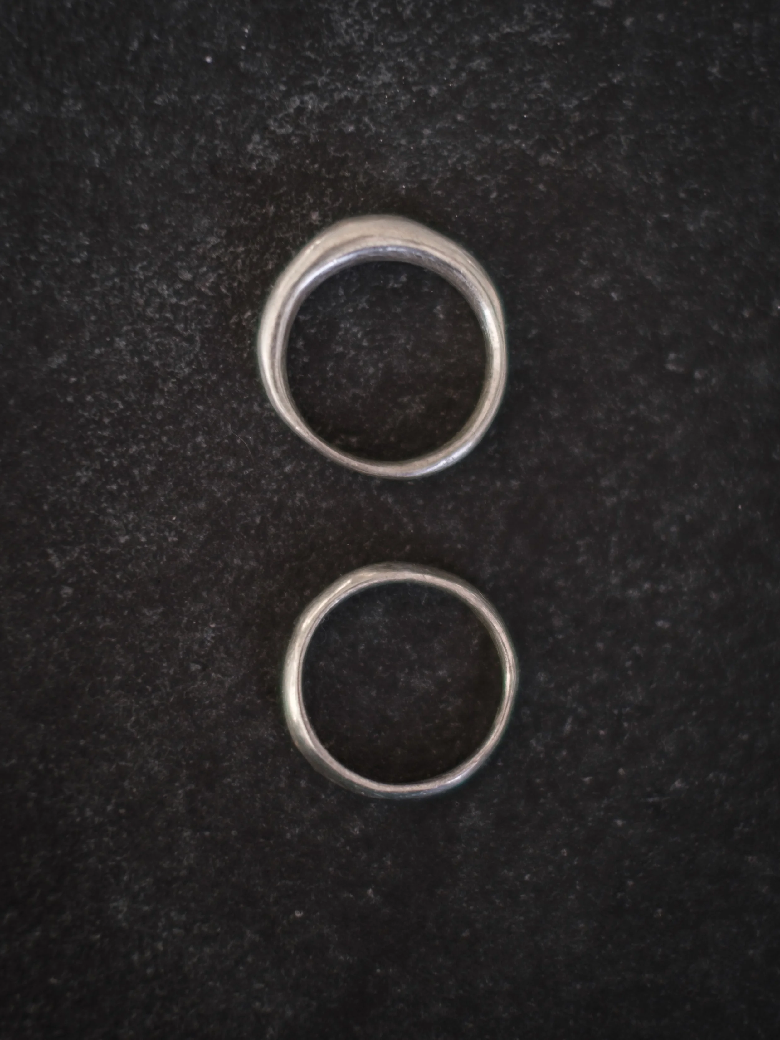 Two silver rings placed on a black textured surface, one above the other.