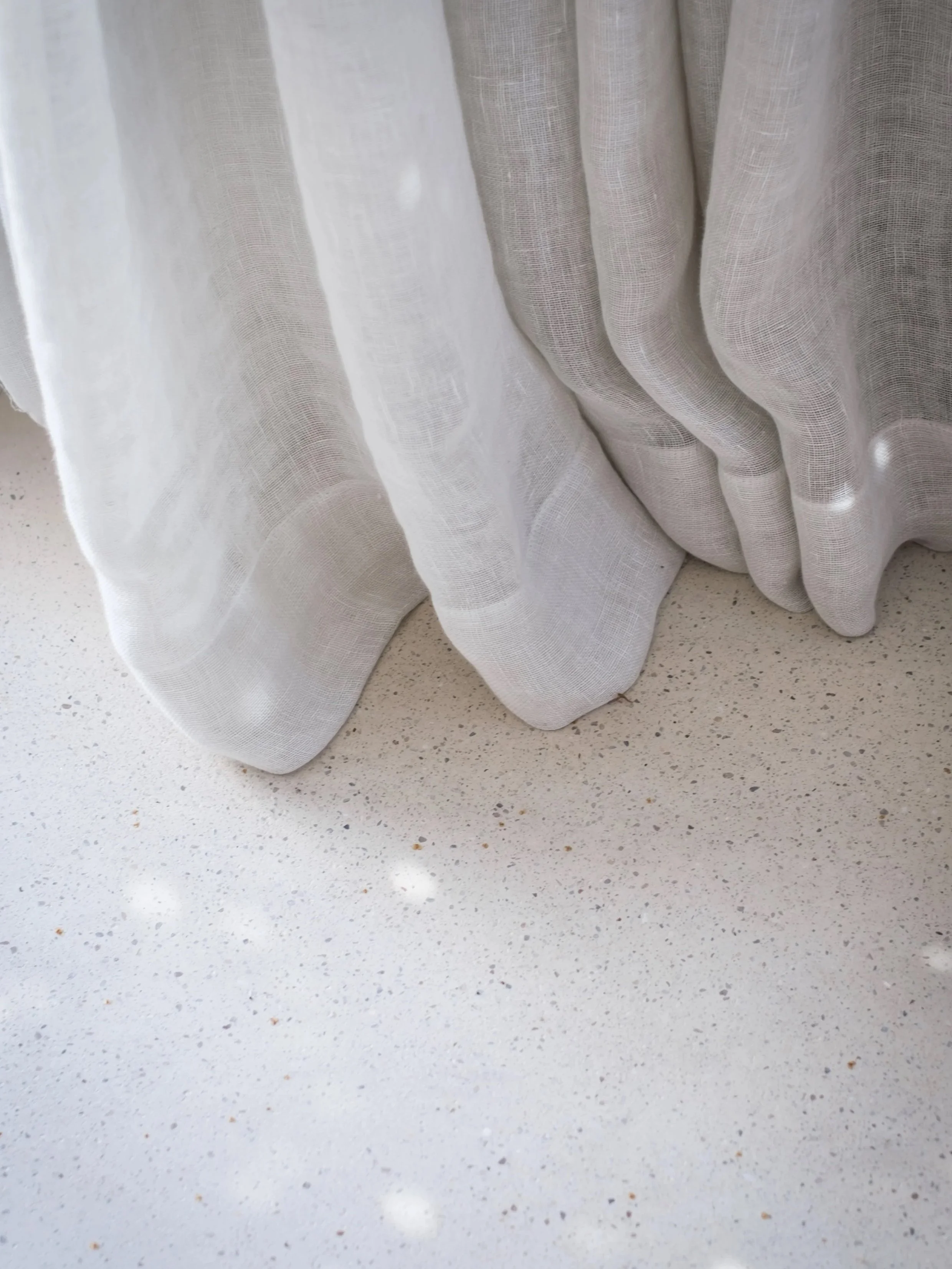 Close-up of white semi-transparent curtain draped over a light-colored speckled countertop.