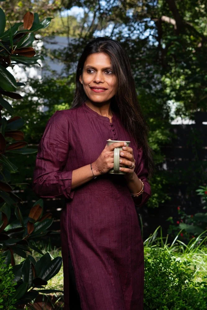 Woman holds a cup of tea in a backyard setting looking off to the side in this editorial style portrait. 