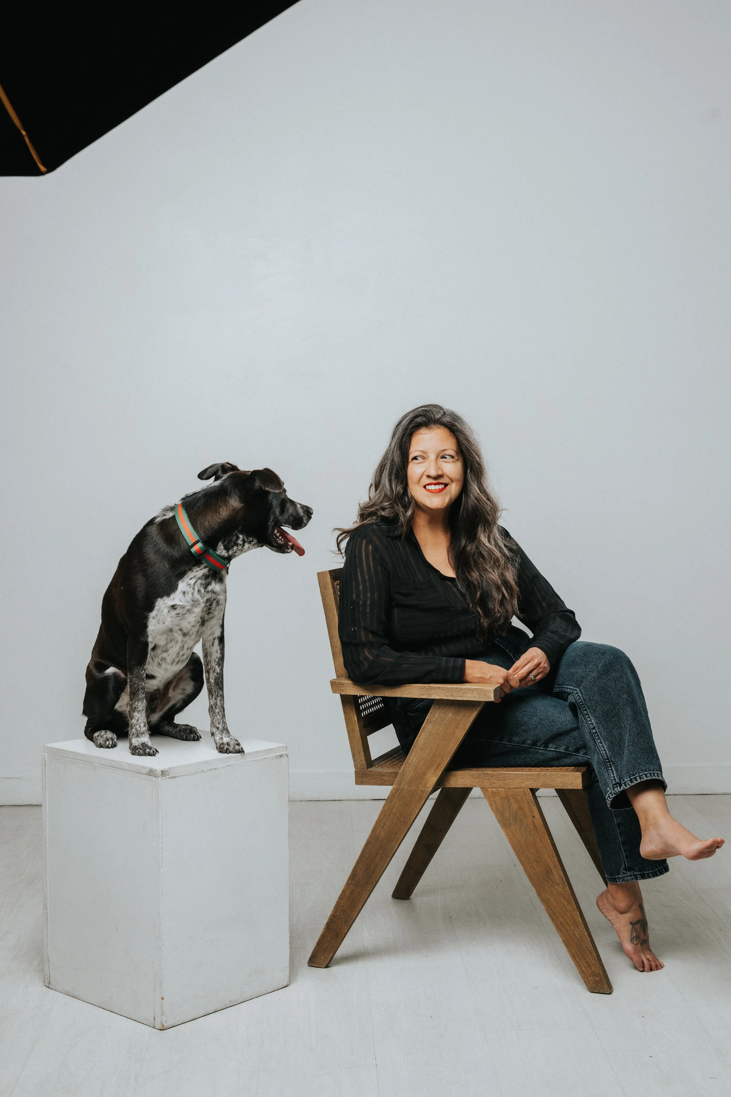 Leandra sits in a chair smiling looking off to the side at her cattle dog who is looking at her. He is perched on a pedestal.Photo by Wag and Pose