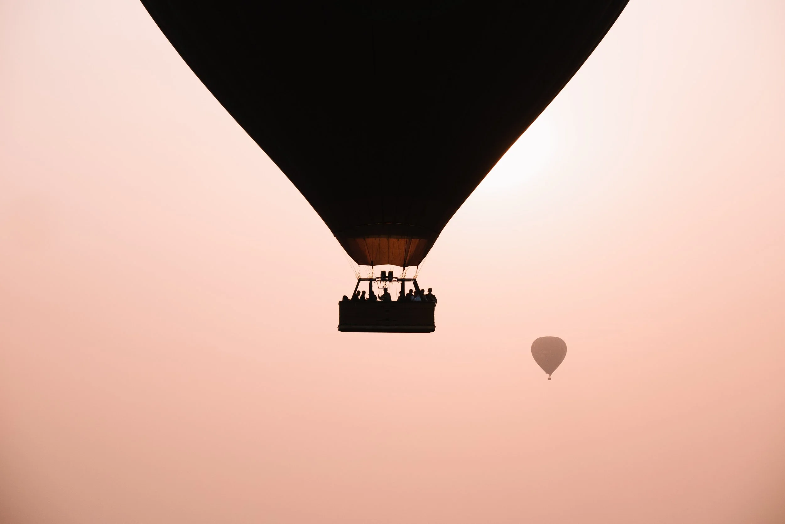 A hot air balloon flying in the sky with a smaller balloon visible in the background, during sunset or sunrise.