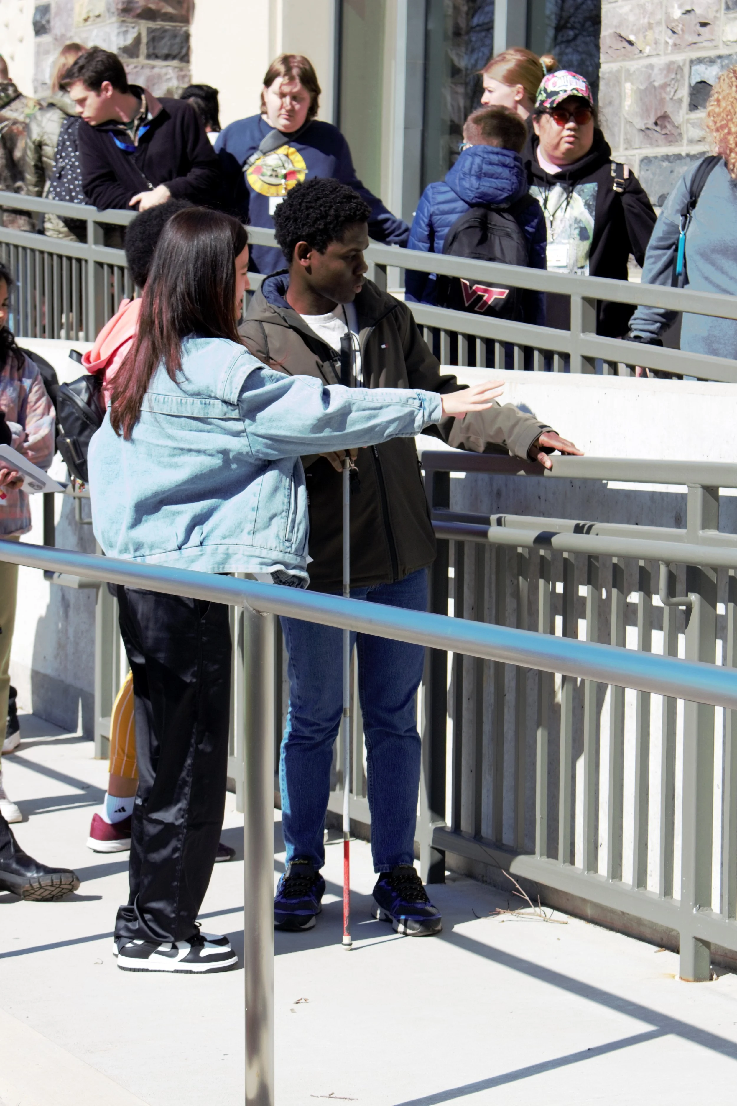 Campus accessibility tour with ADA-specialist architect Joseph Cooley. ID: Mary Ann and Morris stand on a ramp with other participants. Mary Ann points to the railing while Morris investigates it.