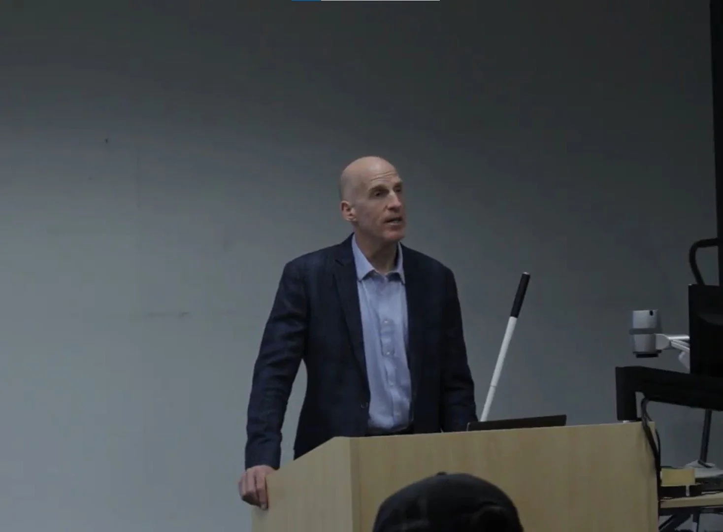 Lecture with architect Chris Downey (2022). ID: Chris stands behind a light wooden podium.