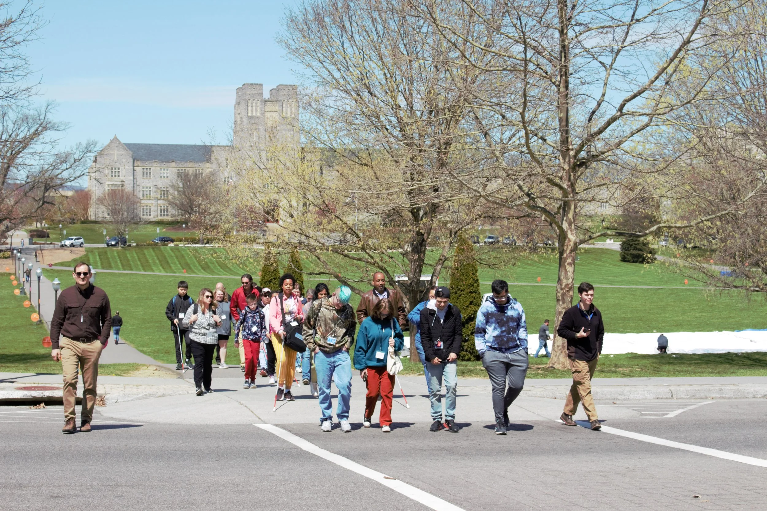 ID: Front-facing view of a large group of participants crossing the street, with the Drillfield and Burruss Hall in the background.