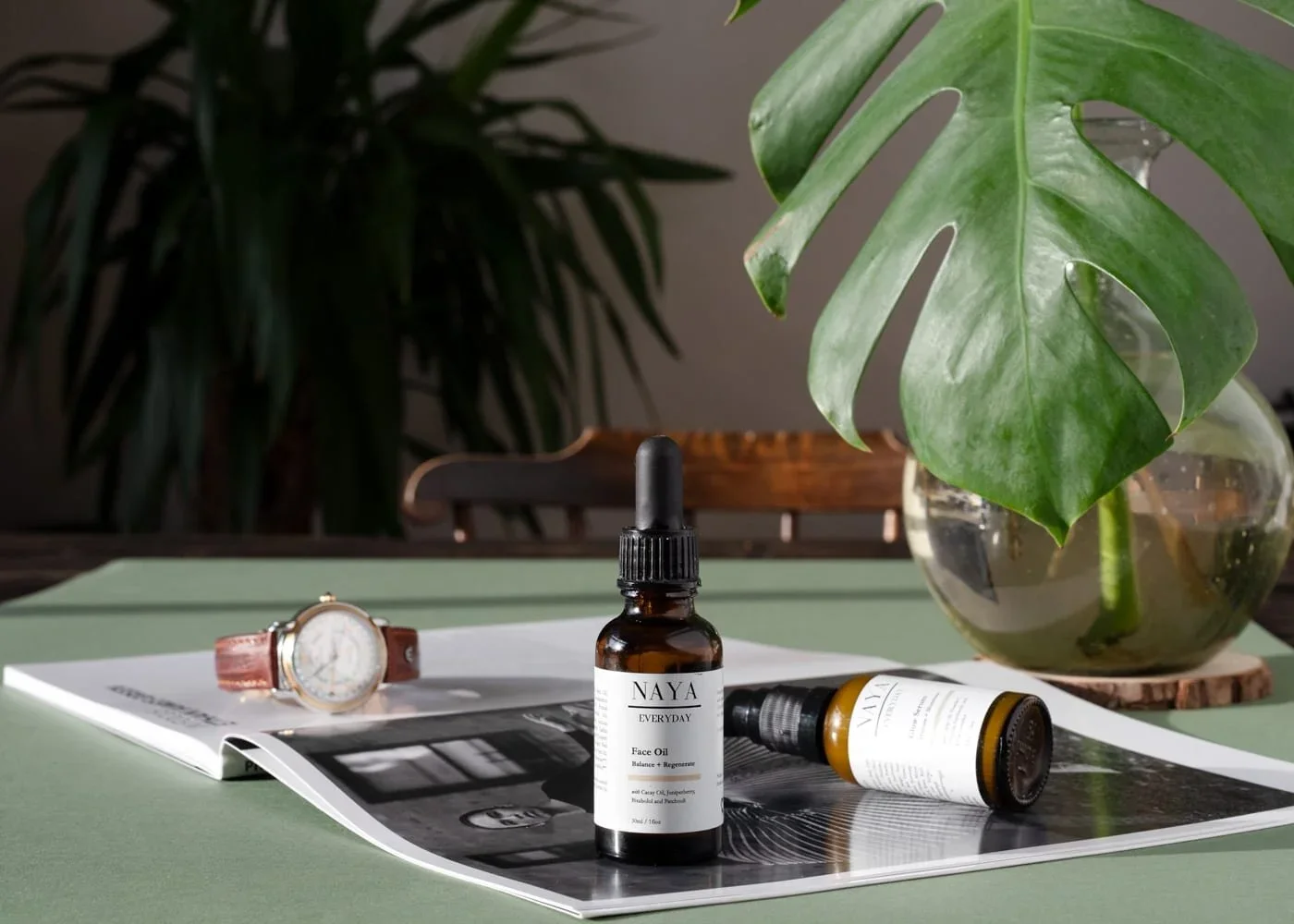 Editorial tabletop scene with glassware, skincare, and Monstera leaf – fresh, botanical and bright.