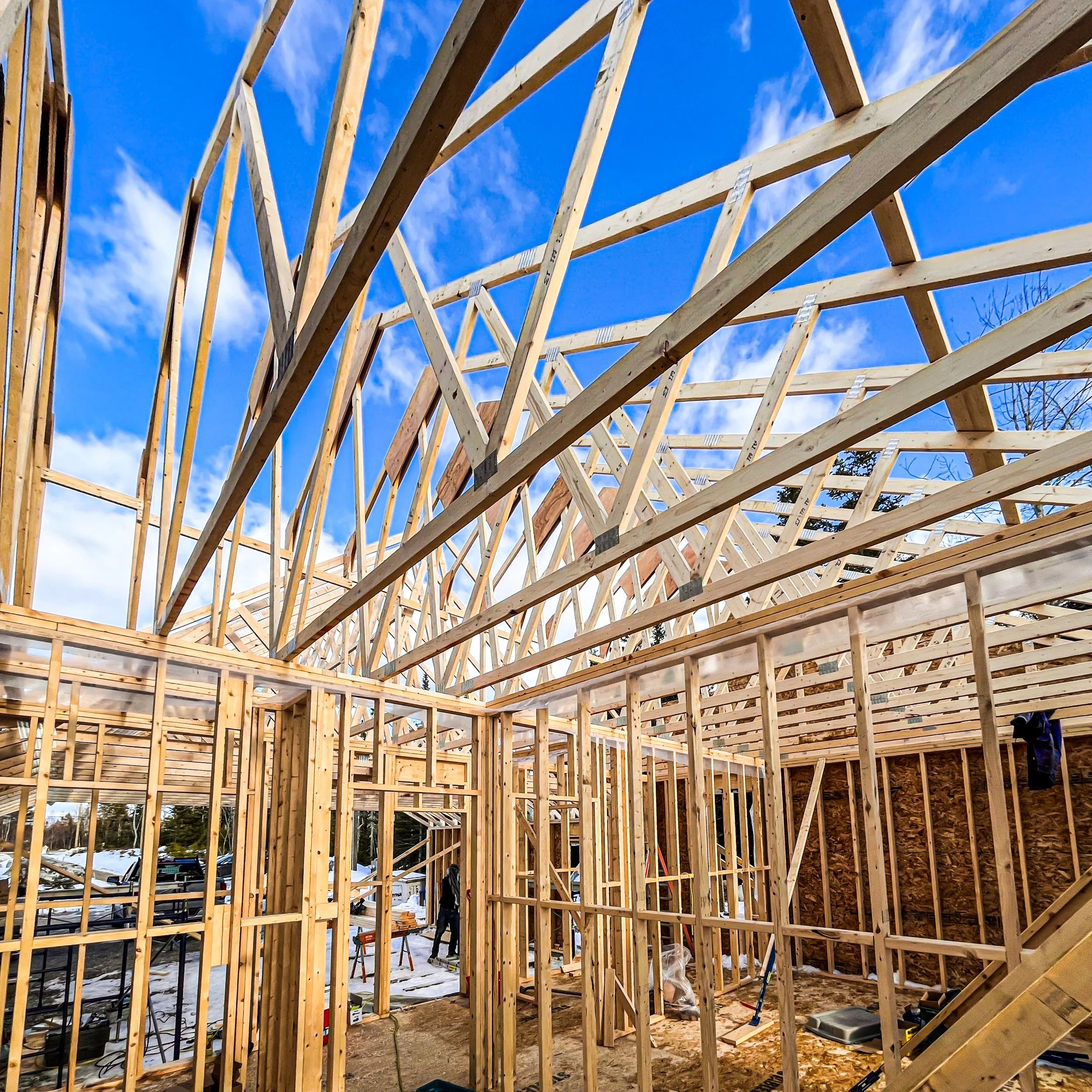 Wooden framing of a building under construction against a blue sky with some clouds.
