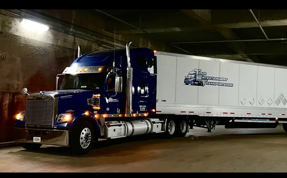 Blue TET truck and branded production trailer inside a venue loading area