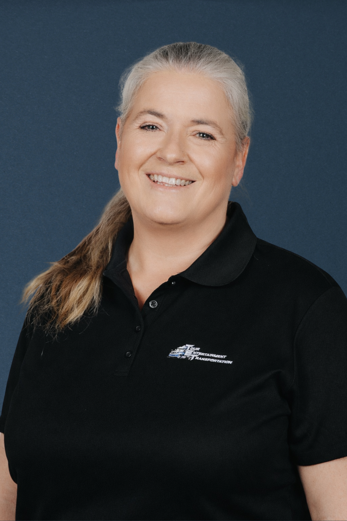 Smile woman in black polo shirt with logo, against dark blue background.