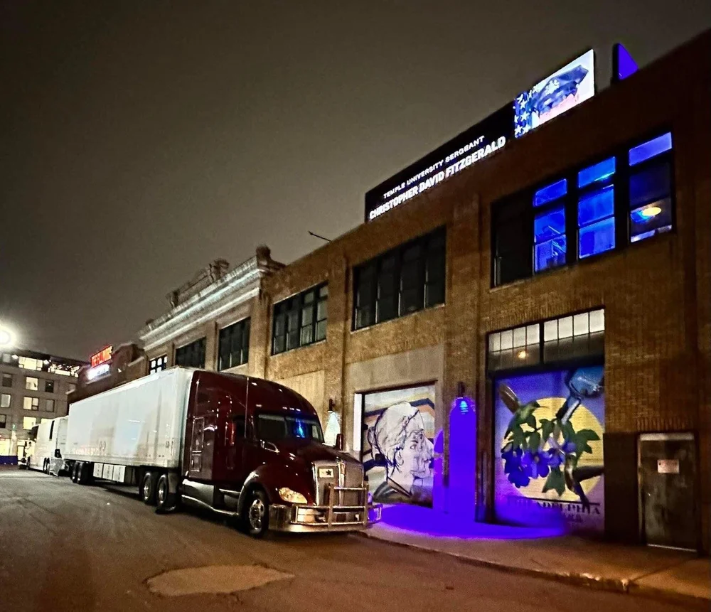 Tour truck and trailer parked outside a venue at night.