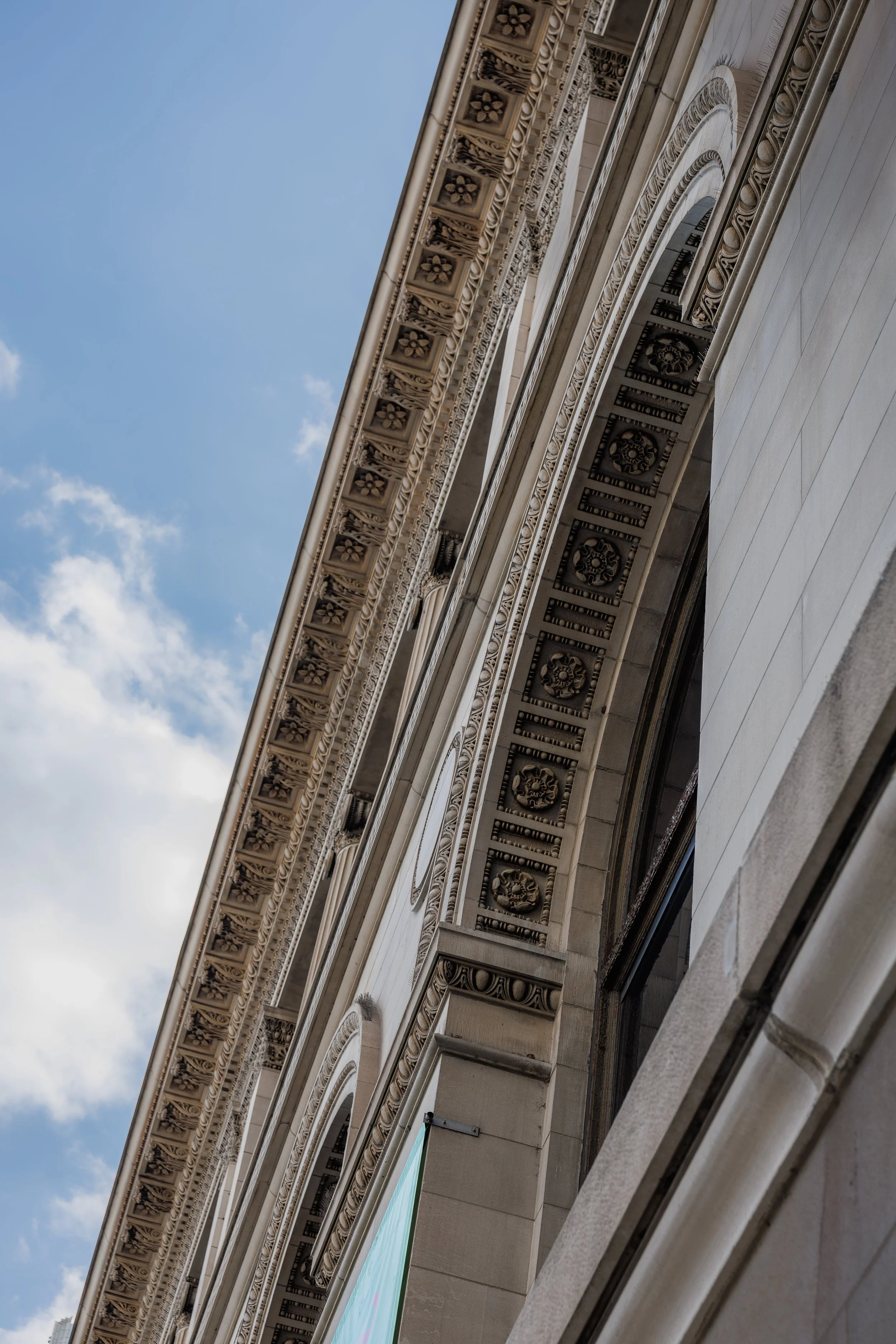 Close-up of an ornate, classical-style building facade with decorative moldings and archways, against a blue sky with scattered clouds.
