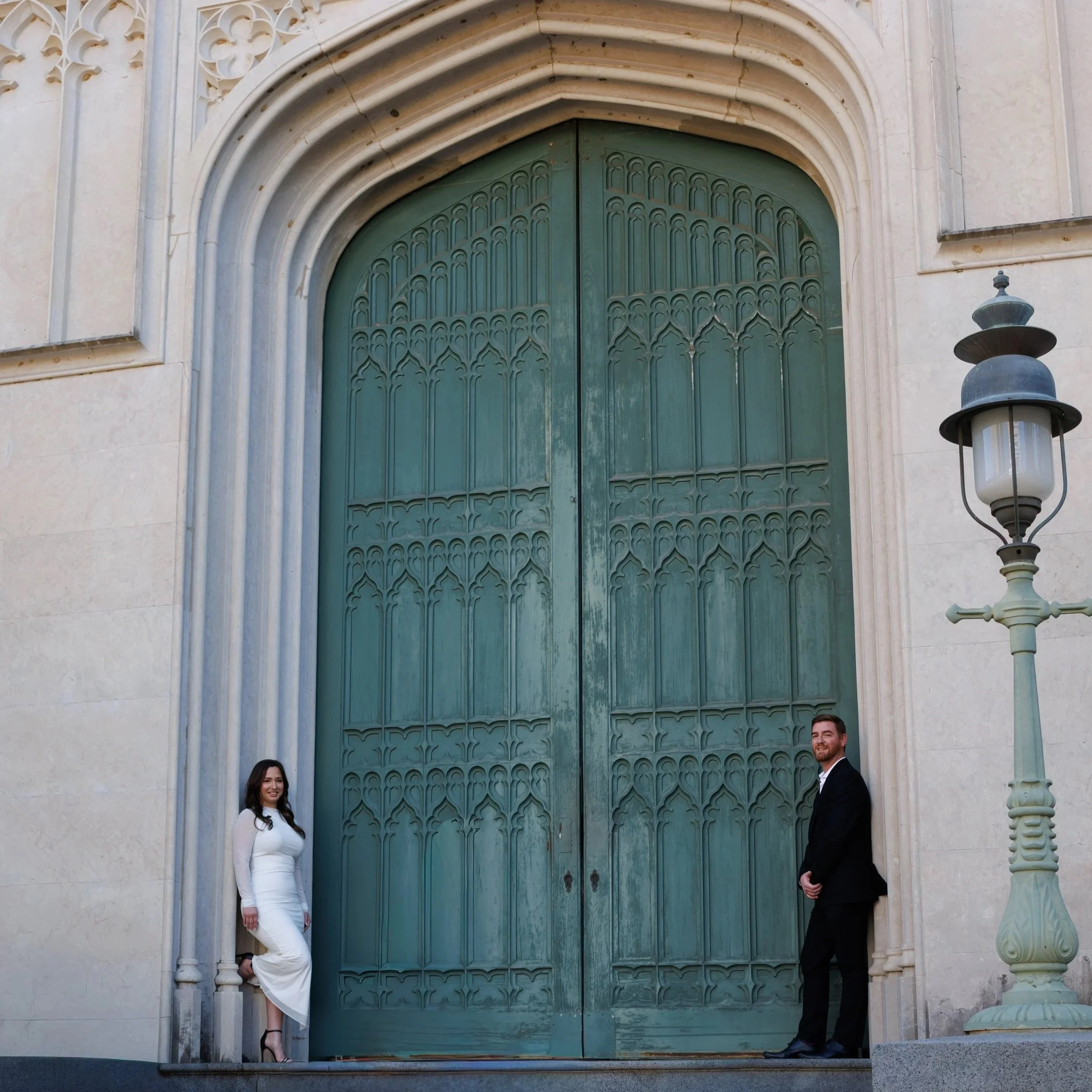A man and a woman dressed in formal attire standing in front of a large ornate green door on a stone building, with a lamp post nearby.
Chicago wedding photographer