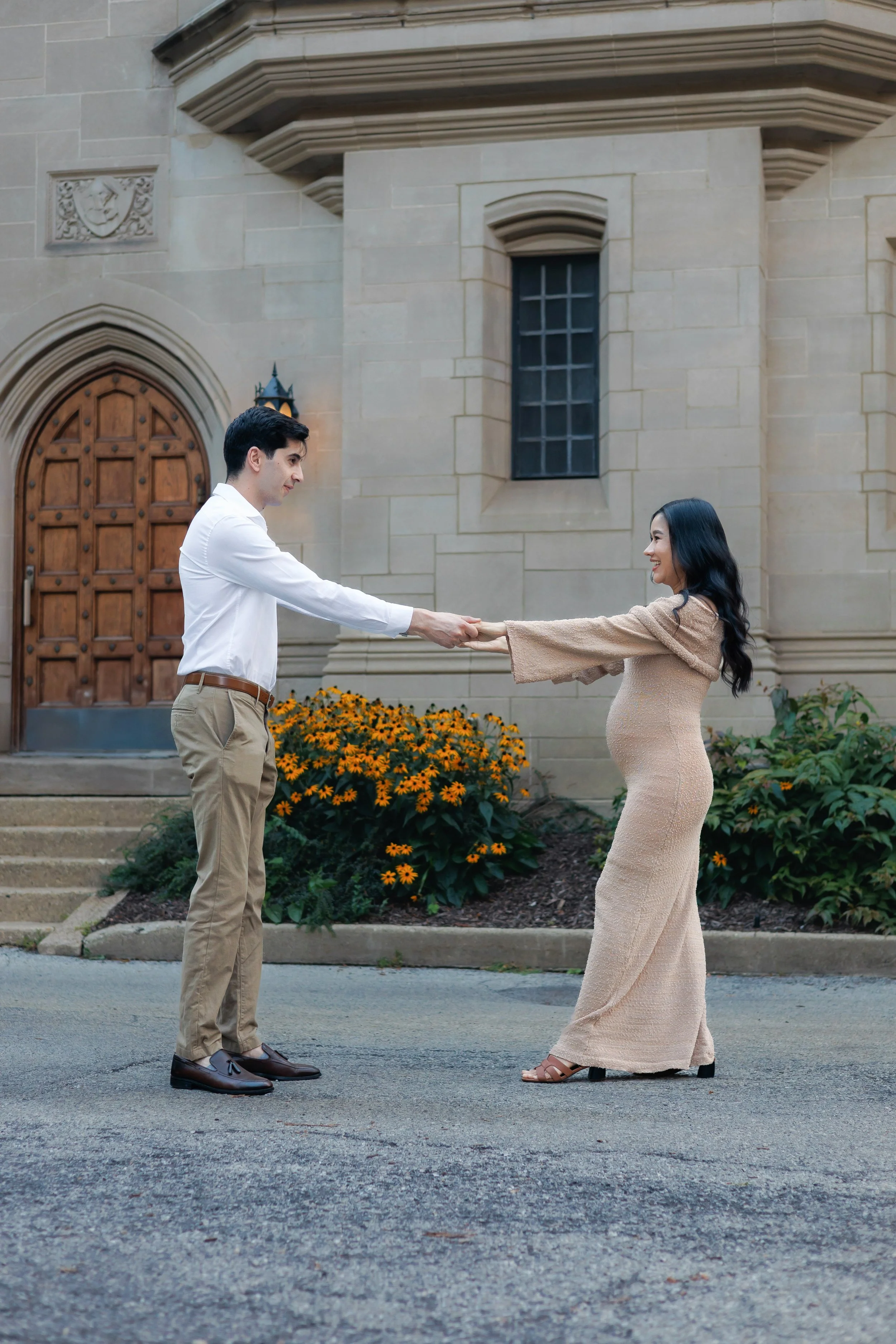 Pregnant woman in orange dress holding belly outdoors next to a tree.