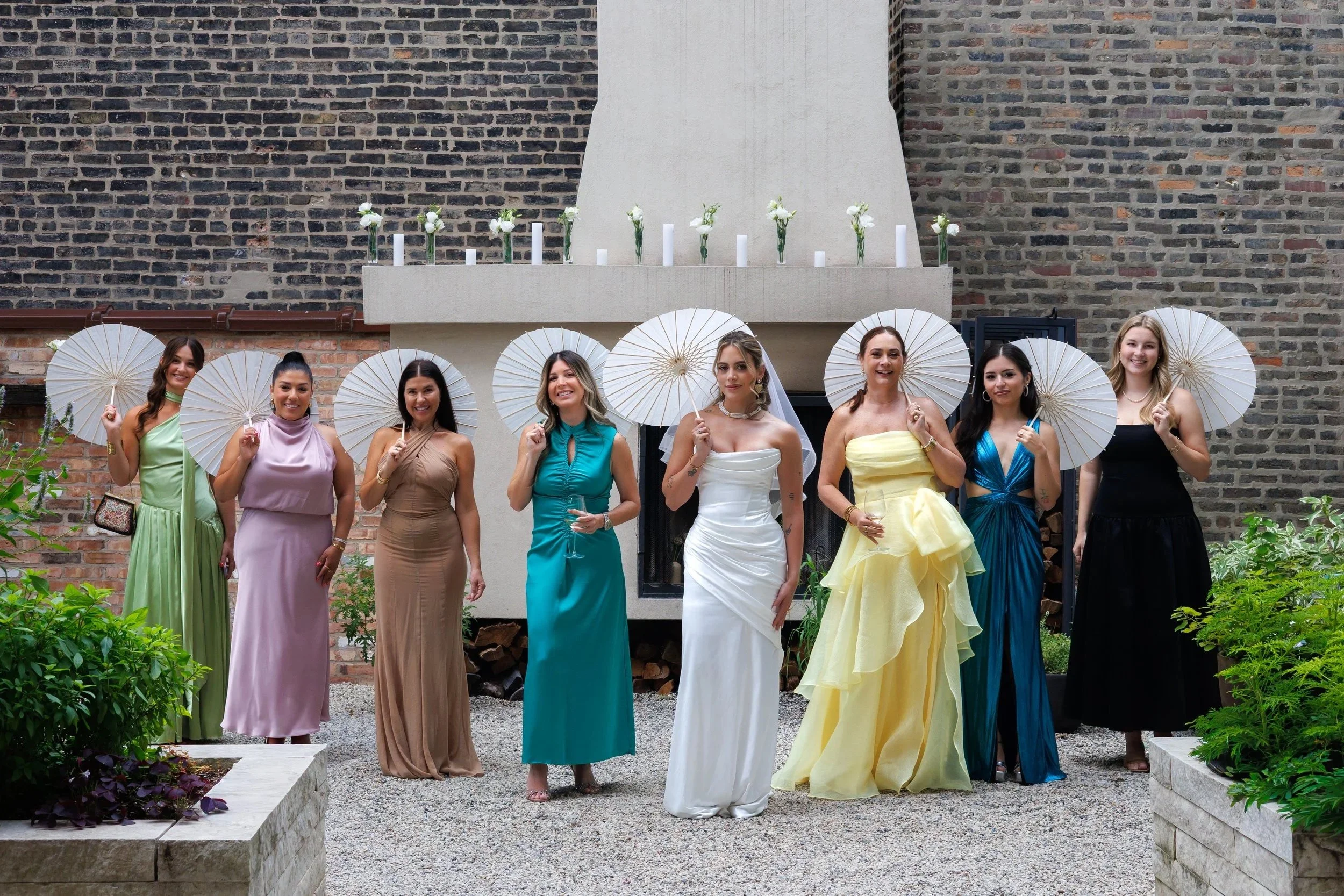 Chicago wedding photographer capturing a bridal party holding white umbrellas in front of a brick wall, stylish and candid group wedding photo