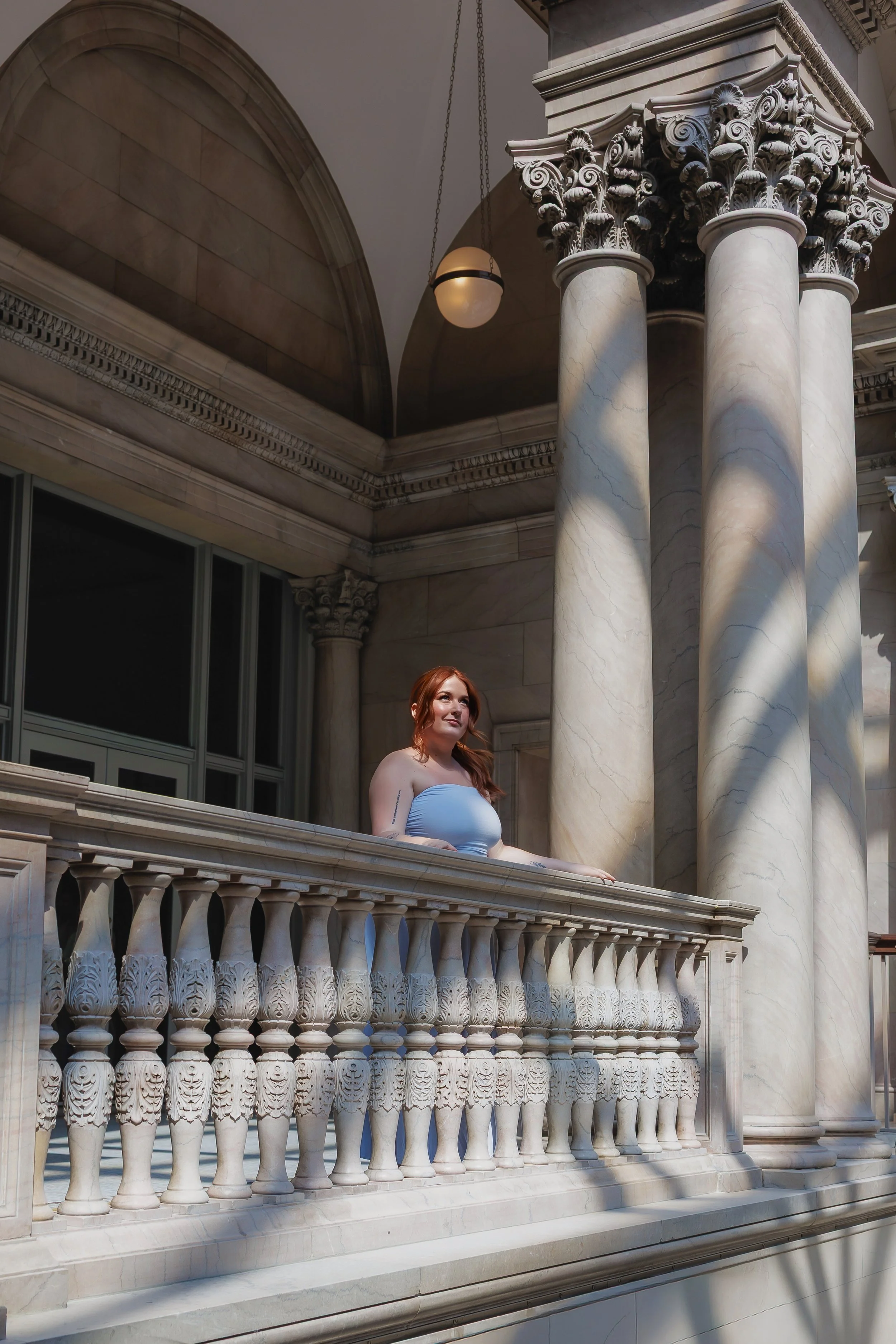 A woman in a light blue dress stands, observing the view of the main area in the Art Institute of Chicago with large columns around her.