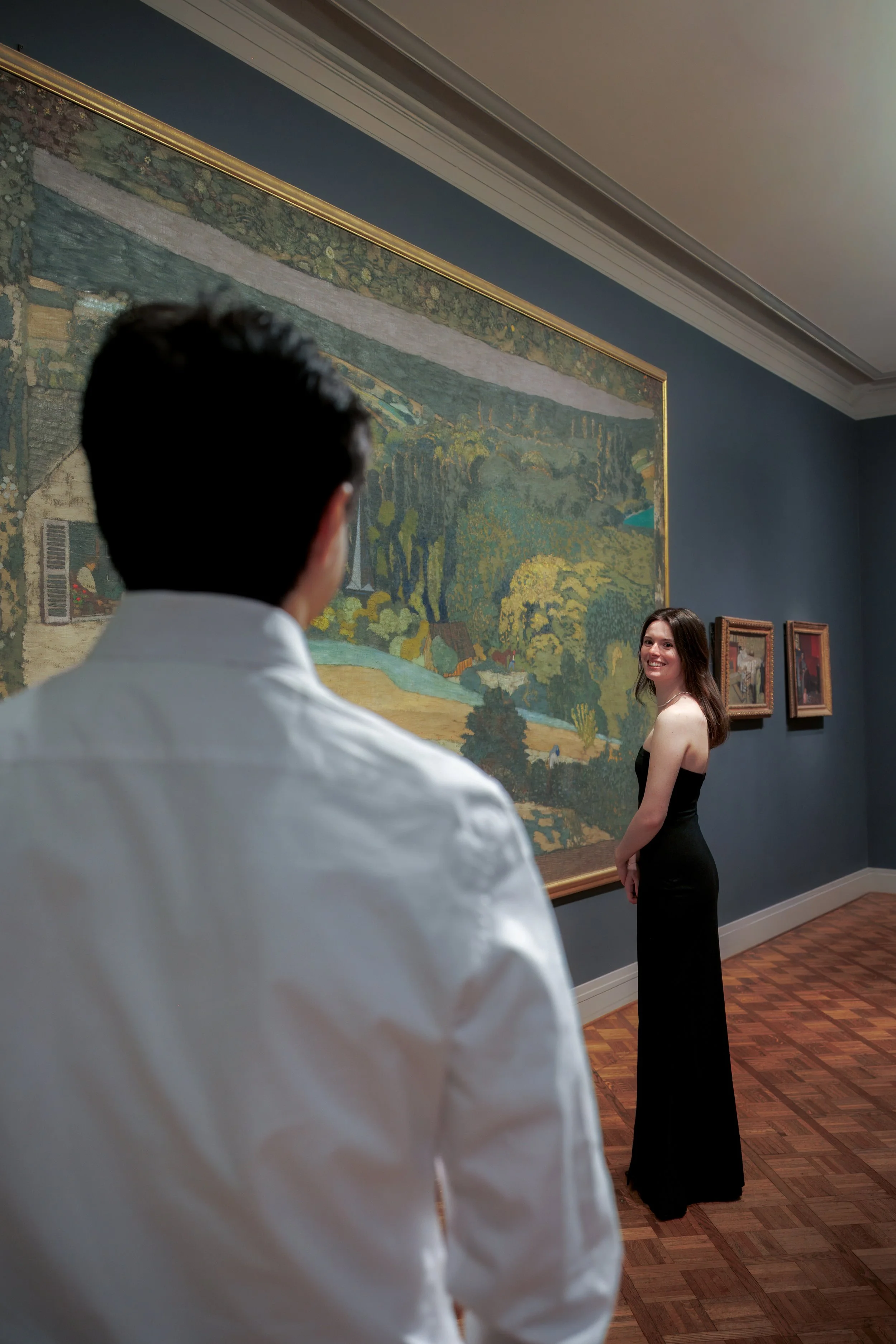 Woman smiling back at her partner inside the Art Institute of Chicago gallery, framed by blue walls and a sweeping landscape painting.